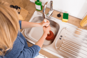 A homemaker plunging the kitchen sink drain with a plunger
