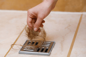 A person removing hair from the shower drain
