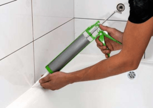 A plumber re-caulking bathroom tiles with a caulk gun